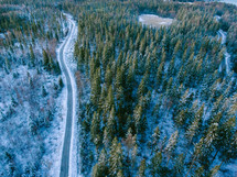aerial view over a highway through a snowy forest 