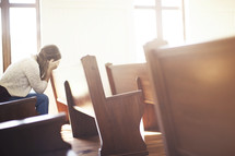 a woman siting in a church pew hiding her face 