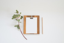 eucalyptus twig, clipboard, blank paper, pencil 