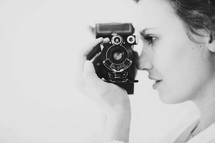 Woman holding a vintage camera to her face.