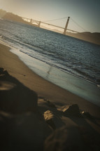 tide washing onto a shore and a bridge over a bay
