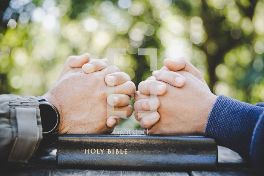 Hands folded on Bible in prayer