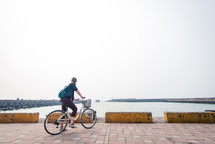 woman riding a bike on pavers near a harbor 