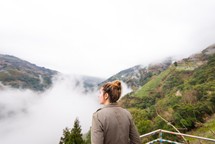 a woman looking out at rising fog in a valley 