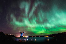 man with raised hands under an aurora 