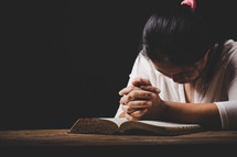 Woman praying with hands on her Bible
