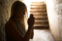 a woman with praying hands sitting in a hallway 