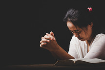 Asian woman praying with hands folded together with an open Bible