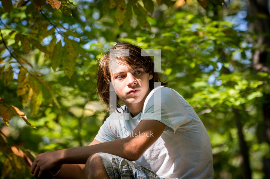 teen boy squatting in a forest 