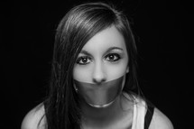 Speak no evil. A woman with her mouth covered with duct tape.