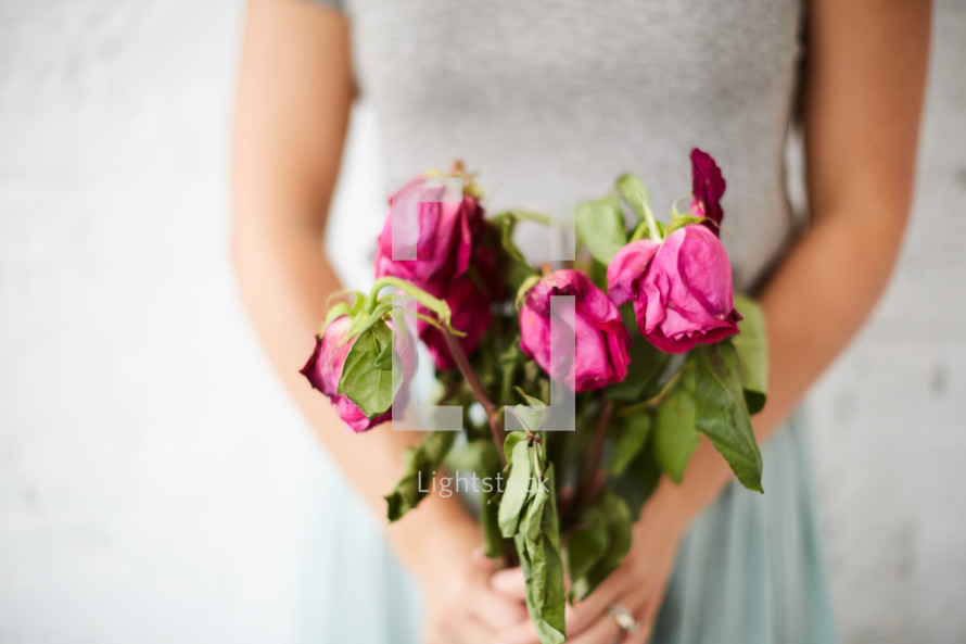 a woman holding a bouquet of wilting roses 