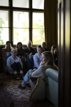 a close up of a young woman listening in a group of young people inside a room filled with natural light