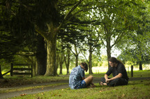 two young men sitting together praying in the grass in a beautiful setting
