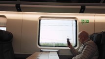Elderly man is traveling by train taking picture with phone
