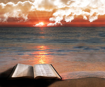 Open Bible on a beach at sunrise as the tide washes over it 