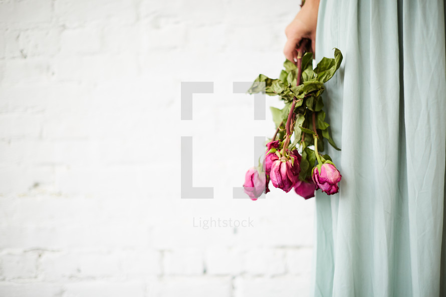 a woman holding a bouquet of wilting roses 