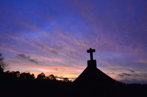 silhouette of a cross on a roof at sunset 