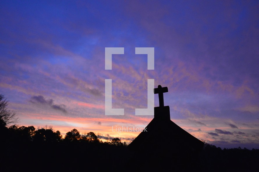 silhouette of a cross on a roof at sunset 