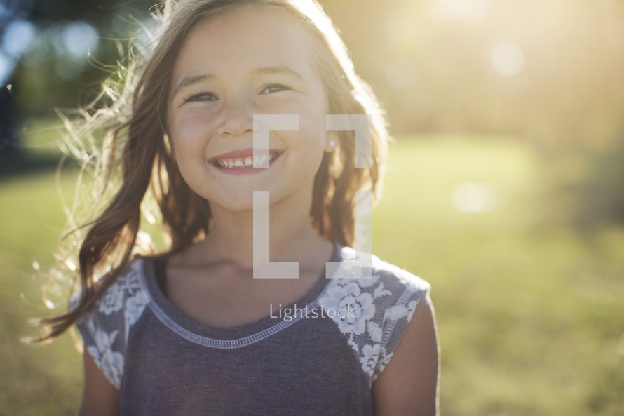a smiling little girl standing outdoors.