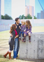 family portrait with daughters sitting on a concrete wall 