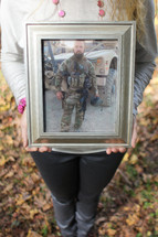A woman holding a framed photo of a soldier.