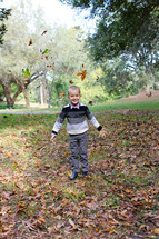 A little boy throwing leaves in the air.