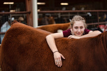 Country girl relaxes contentedly while she leans on the heifer she raised from a calf. 