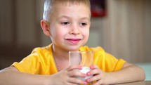Healthy food. Happy little boy hold glass of milk. Kid cute boy sit at table with plate and food. Healthy nutrition. Drink milk.