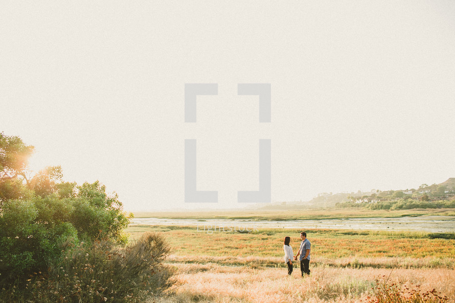 Couple standing in a meadow holding hands.