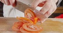 Slow motion close up of a chef knife slicing a tomato