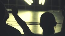 Silhouette of an audience at a worship service with arms raised.