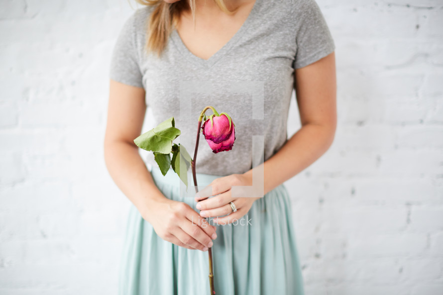 a woman holding a wilting rose 
