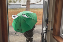 a boy walking out a door holding an umbrella 