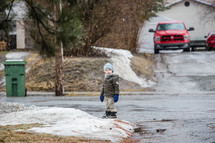 a child standing at the end of a driveway with falling snow 
