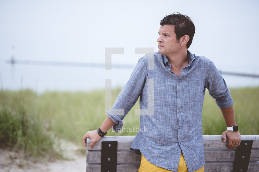 man leaning against a bench on a beach 