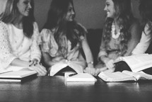 women's group holding hands in prayer on a couch and reading Bibles 