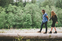 A man and woman walking along a log in a forest.
