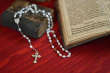 rosary on the pages of  a very old ancient book in old German lettering on red wooden table