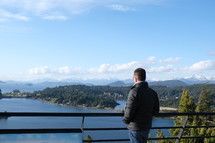 a man looking over a railing at a lake 