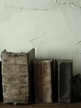 Antique books on a shelf against a stucco wall.