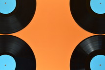 four old black vinyl records with blank cyan labels on orange background
