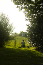 A person sitting on a bench looking out over a green pasture