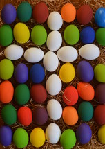 White cross between colorfully painted Easter eggs.
