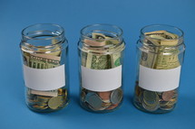 three savings jars full of money with blank labels on cyan background