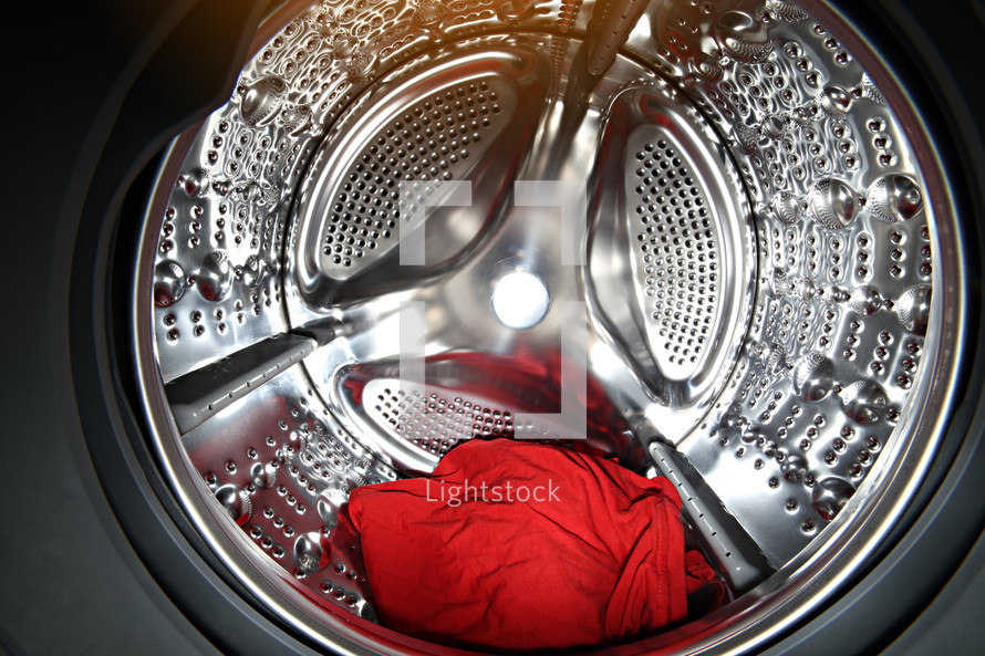 View of the tumble dryer or washing machine drum with red clothes inside. Laundry day. Daily household chores. Domestic and Household Appliance. Home Innovation