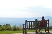 father and son sitting on a bench on a mountaintop 