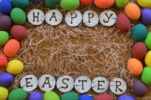 HAPPY EASTER burned into pieces of wood surrounded with colorful eggs on straw. 
