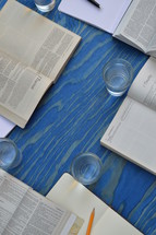 small group bible study with different bibles, notebooks, pens and glasses on a blue wooden table