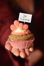 Woman offering a cupcake with pink hearts and a sign saying JE T'AIME, which means: I LOVE YOU. 