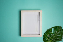 Blank white frame and leaf on turquoise background